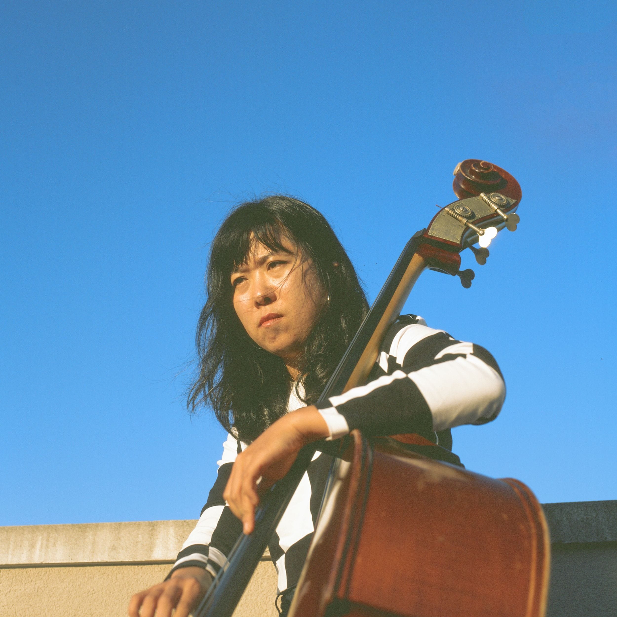 A photo of Jeong Lim Yang playing the upright bass against a blue sky