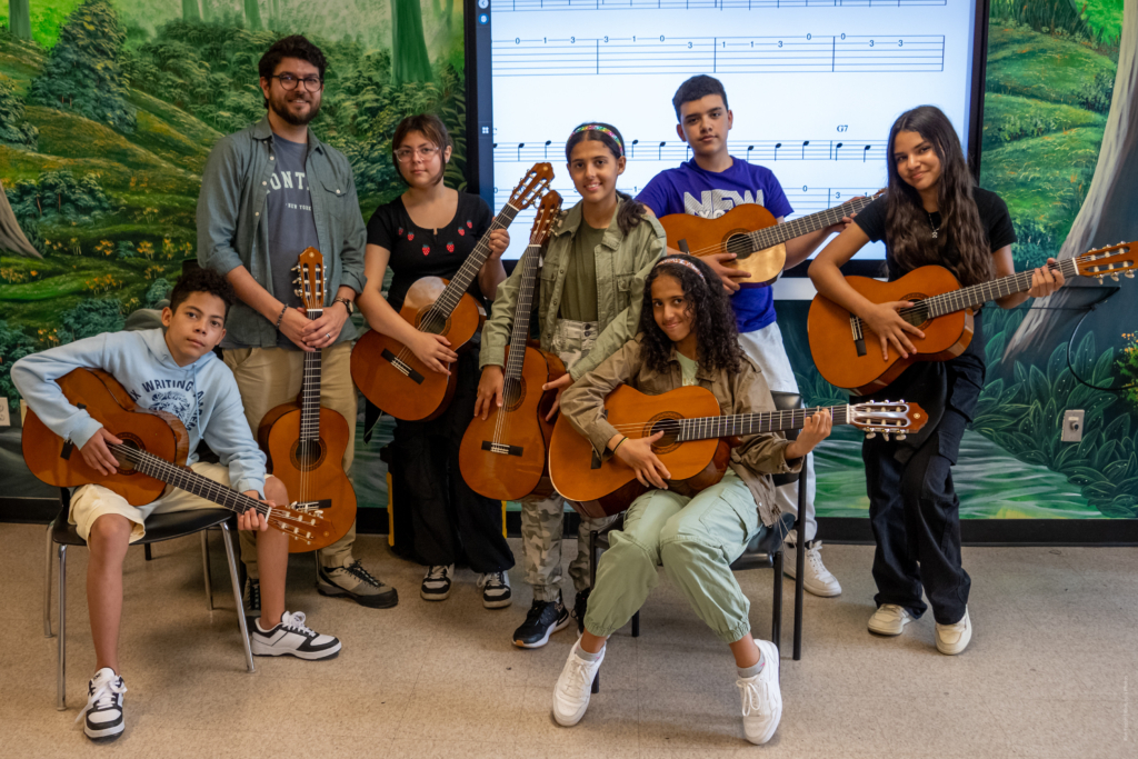 Students in a class at IS 235 posing with their guitar teacher and their guitars