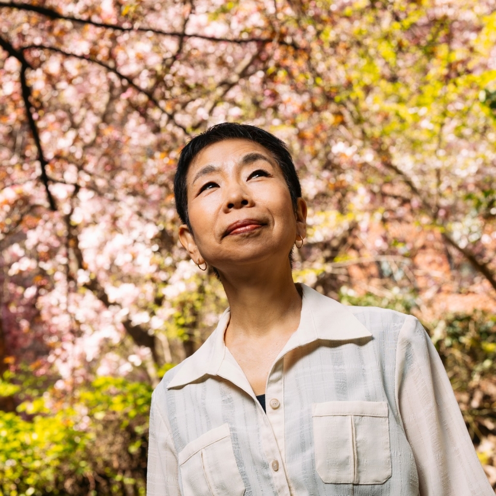 A photo of Yoko Yates with cherry trees behind her